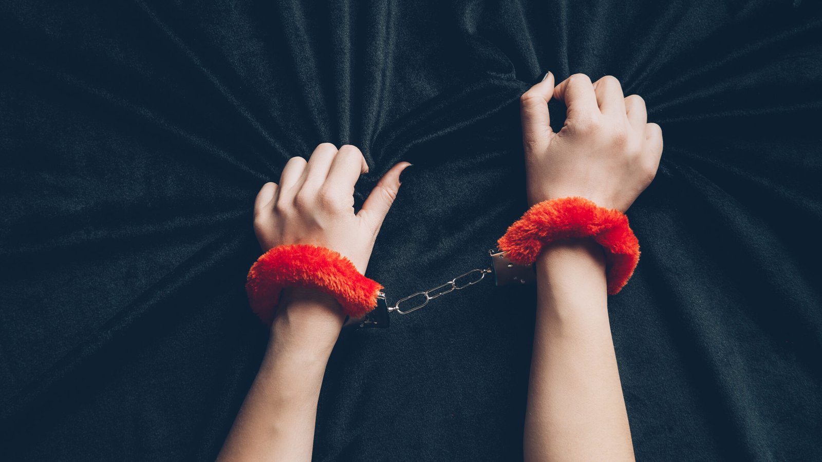cropped shot of woman in red fluffy handcuffs holding black fabric