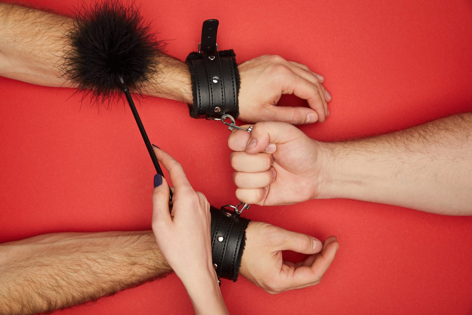 cropped view of men and woman with handcuffs and feather tickler isolated on red