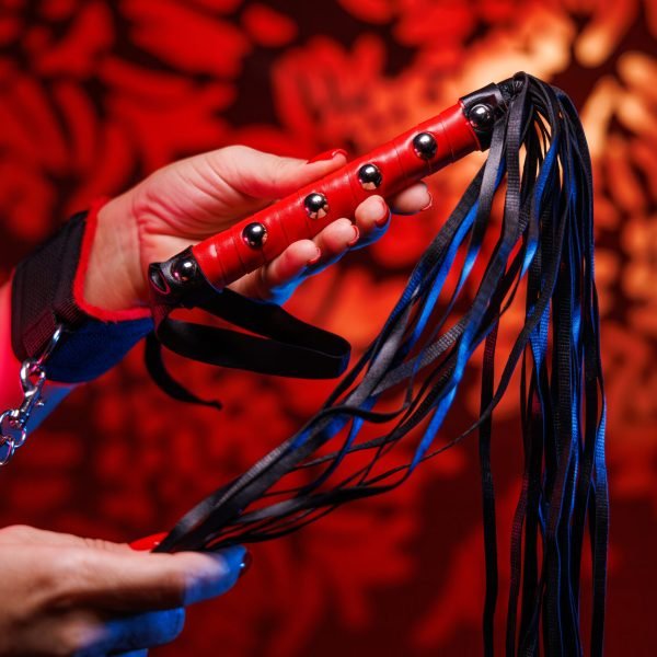 A pair of delicate feminine hands gracefully hold a leather whip featuring a striking red handle Perfectly capturing the essence of sensuality and BDSM exploration