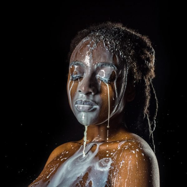 milk spilled on face and naked body of beautiful young african american woman isolated on black