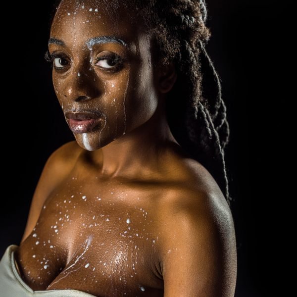 sensual young african american woman with spilled milk on face looking at camera isolated on black